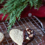 An Embossed Chocolate Dipped Sugar Cookie on a wire rack with others and a green branch in the background