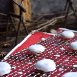 Pfeffernüsse Cookies on a cookie rack with red polka dots below, reindeer looking over, and wood houses and sticks in the background