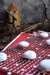 Pfeffernüsse Cookies on a cookie rack with red polka dots below, reindeer looking over, and wood houses and sticks in the background