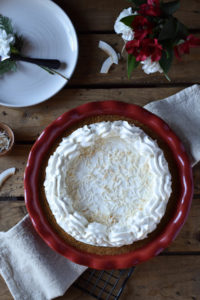 Creamy Cheesecake Pie with Peanut Butter, Honey & Coconut in a decorative napkin with flakes of coconut, a dish of shredded coconut, and a plate with utensils in the background.