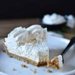 A slice of Creamy Cheesecake Pie with Peanut Butter, Honey & Coconut with a small dish of fresh whipped cream in the background.