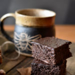 Two stacked Flourless Cocoa Brownies with a cup of coffee in a bee cup in the background.