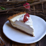 A slice of Classic Cheesecake Pie with Strawberry with wood twigs and red flowers.