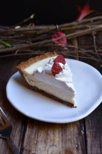 A slice of Classic Cheesecake Pie with Strawberry with wood twigs and red flowers.