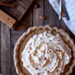 An overview of Butterscotch Pie with Spiced Rum Whipped Cream with utensils and almonds in the background.