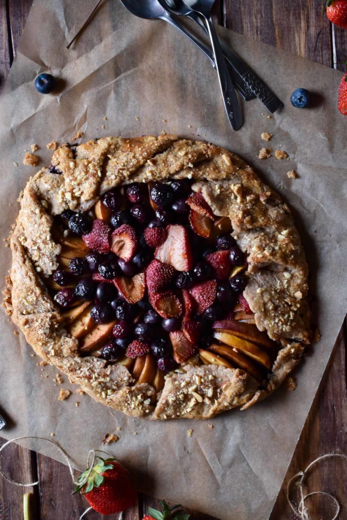 Rustic Fruit Galette with silverware, berries, and flowers in the background.