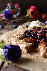 Rustic Fruit Galette with silverware, berries and flowers in the background.