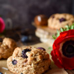 Blueberry Coconut Clove Scones with blueberries and red and blue flowers in the background.
