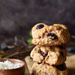 A stack of three Blueberry Coconut Clove Scones with a bowl of coconut to the side and blueberries in the background.