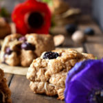 Blueberry Coconut Clove Scones with blueberries and red and blue flowers in the background.