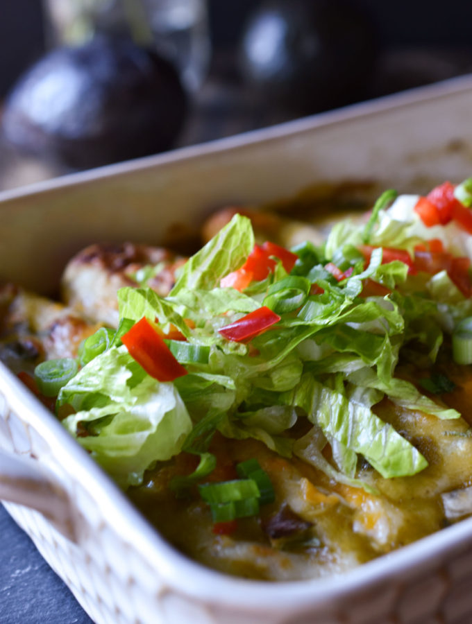A dish of Sweet Potato Black Bean Enchiladas topped with lettuce, bell peppers, and green onions
