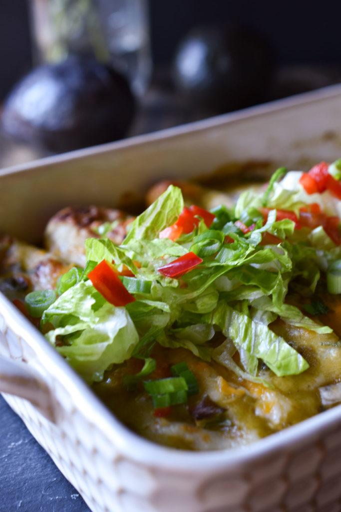 A dish of Sweet Potato Black Bean Enchiladas topped with lettuce, bell peppers, and green onions