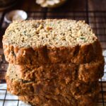 Sliced and stacked 100% Whole Grain Zucchini Bread with a flower in the background.