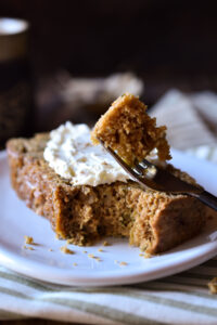 A slice of 100% Whole Grain Zucchini Bread with cream cheese on top and a bite taken.