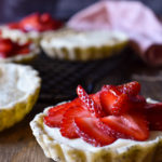 A Strawberry with Vanilla Bean Cream Tart with a pink napkin and more tarts in the background.