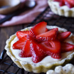A Strawberry with Vanilla Bean Cream Tart with a pink napkin and more tarts in the background.