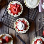 An overview of five Strawberry with Vanilla Bean Cream Tarts on and off a baking rack..