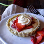A Strawberry Tart with Vanilla Bean Cream with a fork and flowers in the background.