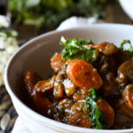 A bowl of Vegetable Bourguignon with flowers in the background