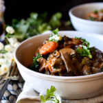 A bowl of Vegetable Bourguignon with another and flowers in the background