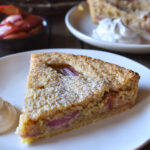 A slice of Bakewell Tart | Roasted Rhubarb with fresh whipped cream on the side and roasted rhubarb in the background.