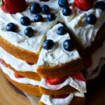 Three layers of fluffed almond and spice cake, whipped cream cheese and colorful fruit, with a slice cut.