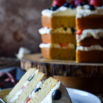 Three layers of fluffed almond and spice cake, whipped cream cheese and colorful fruit, with a slice cut.