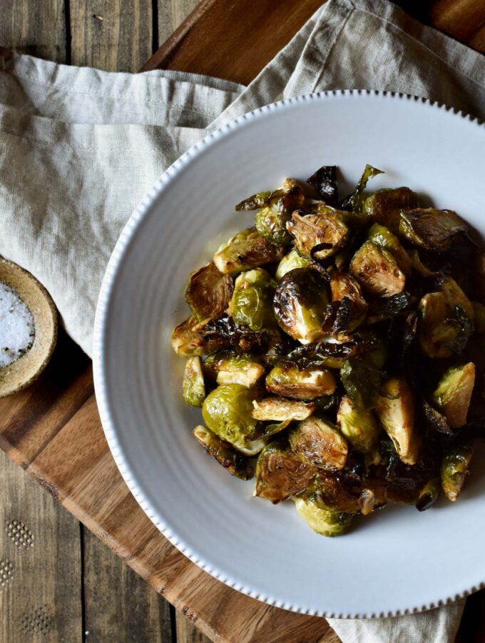 An overview of a bowl of Roasted Garlic Balsamic Brussel Sprouts on a napkin with a small bowl of salt nearby.