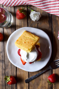 A Cornbread Strawberry Shortcake with a flower and strawberry in the background.