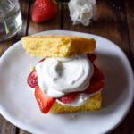 A Cornbread Strawberry Shortcake with a flower and strawberry in the background.