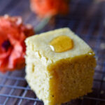 A single piece of Orange Spiced Cornbread with honey on top and orange flowers in the background.