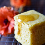 A single piece of Orange Spiced Cornbread with honey on top and orange flowers in the background.