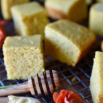 Pieces of Orange Spiced Cornbread with a honey spoon, butter on a wooden knife and orange flower in front.