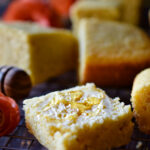 Orange Spiced Cornbread with butter and honey on top and a bunch of pieces behind.