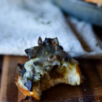 A Sautéed Mushroom Garlic Crostini with a bite take out and more in a tin pan in the background