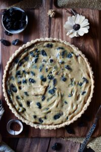 An overview of Sour Cream Raisin Tart with raisins, a dried flower and spices surrounding.
