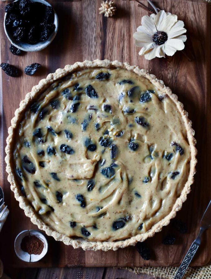 An overview of Sour Cream Raisin Tart with raisins, a dried flower and spices surrounding.