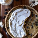 An overview of Sour Cream Raisin Tart with raisins, a dried flower, raisins, and whipped cream surrounding.