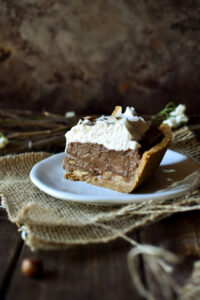 A slice of Chocolate Banana Coconut Cream Pie plated with rustic sticks behind.
