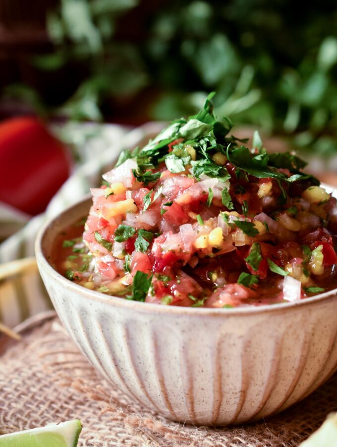 A bowl of Raul's Fresh Mango Salsa Fresca with cilantro, tomato and lime in the background.